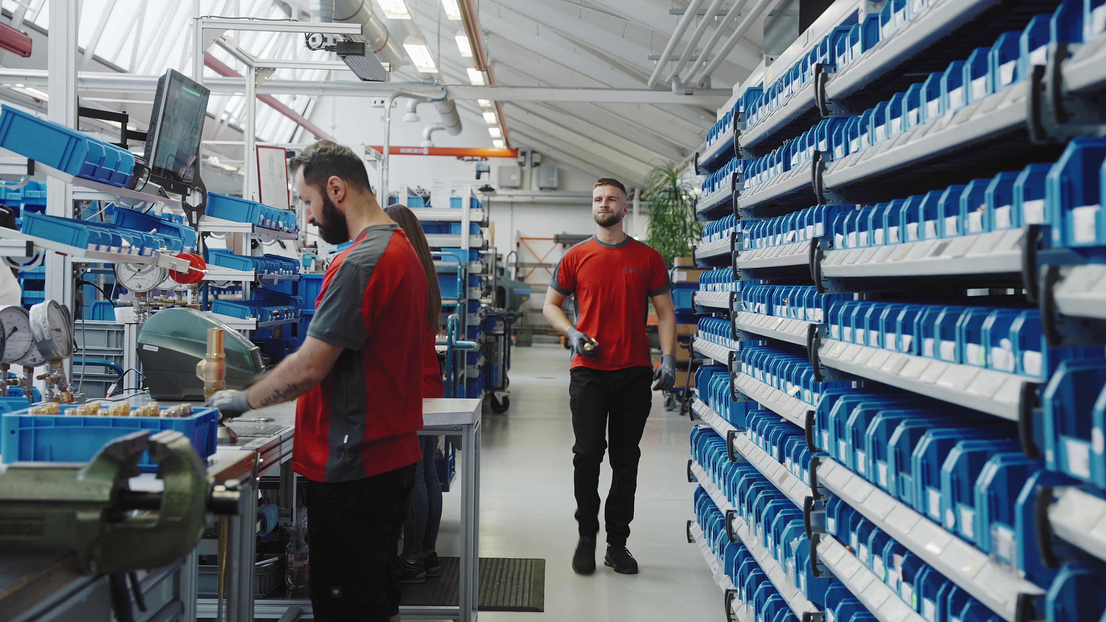 zwei Arbeiter in roter Arbeitskleidung in einer Produktionshalle