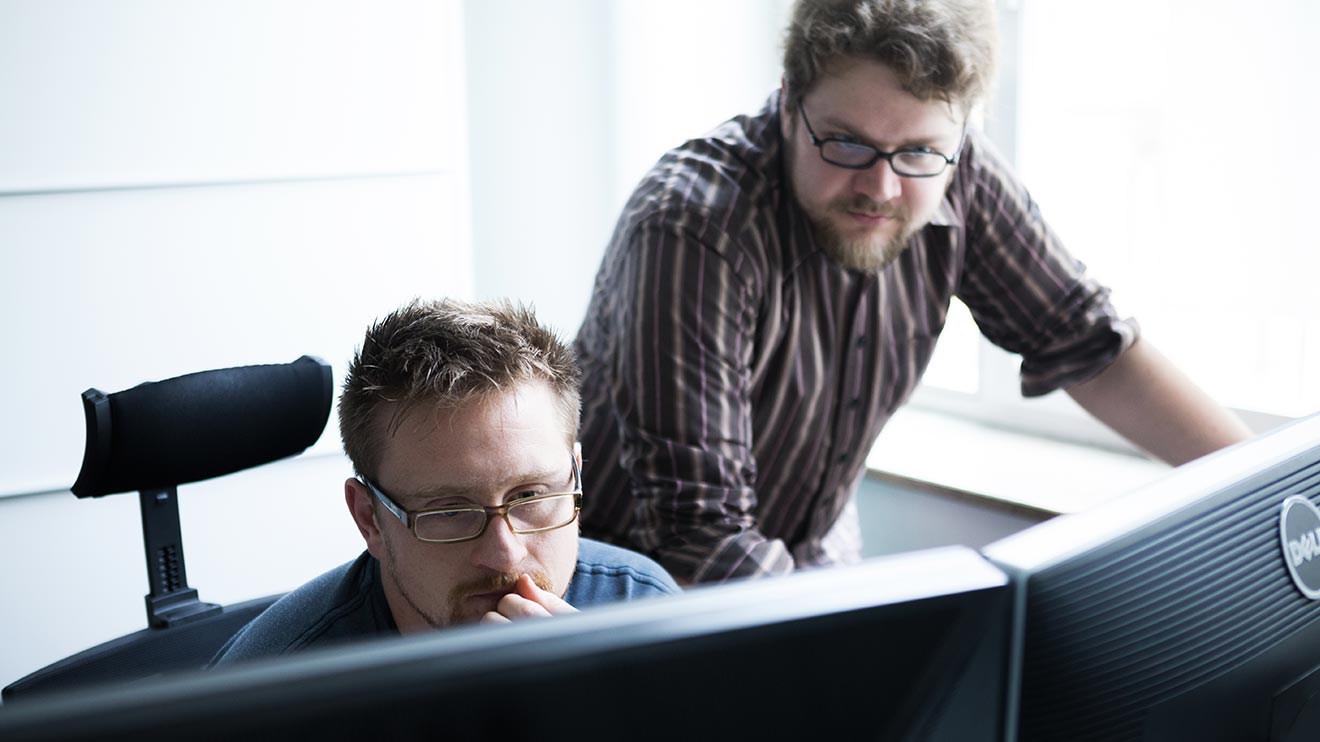 Zwei Männer schauen auf zwei Monitoren in einem Büro