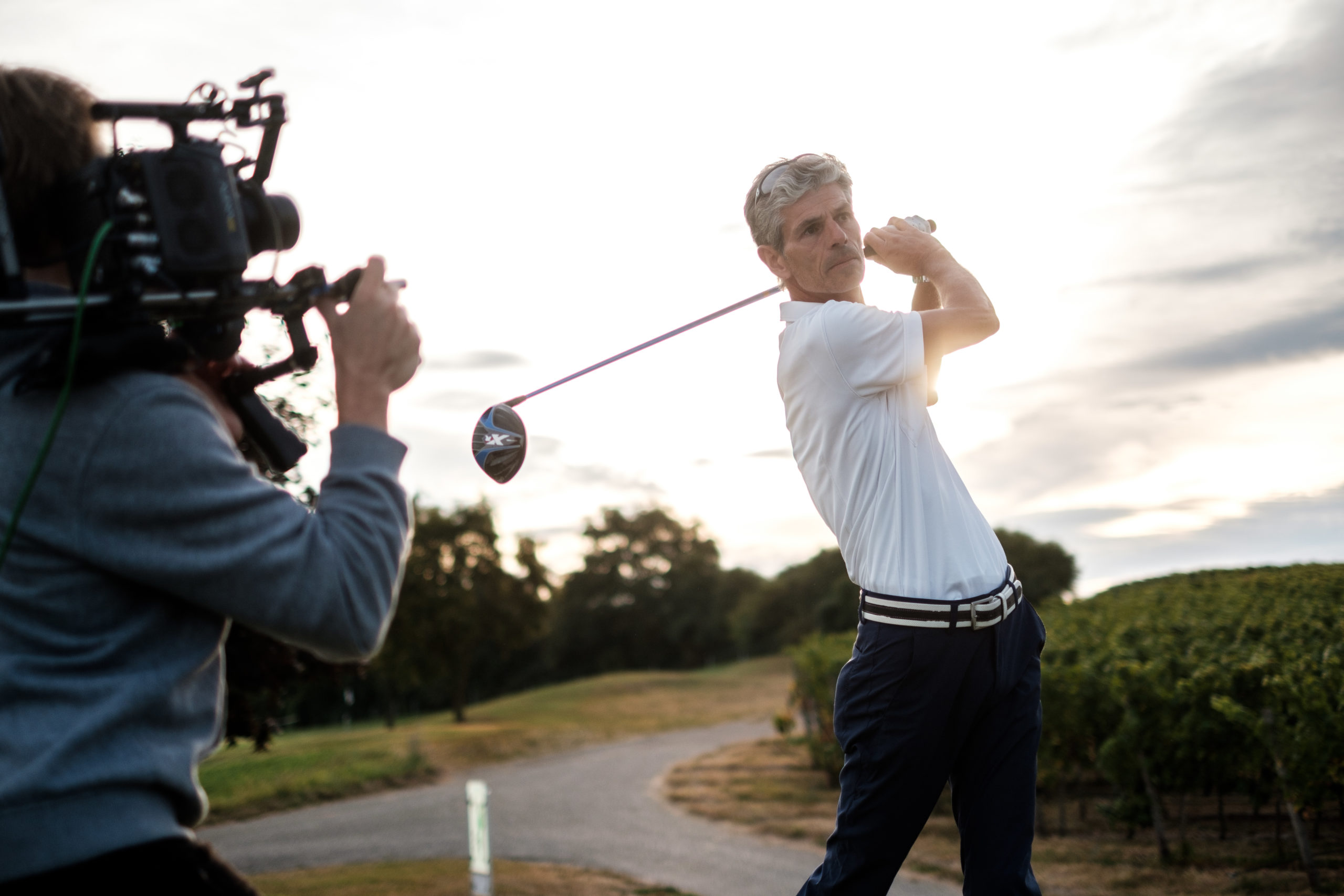 Golfer in weißem Polohemd wird von einem Kameramann efilmt