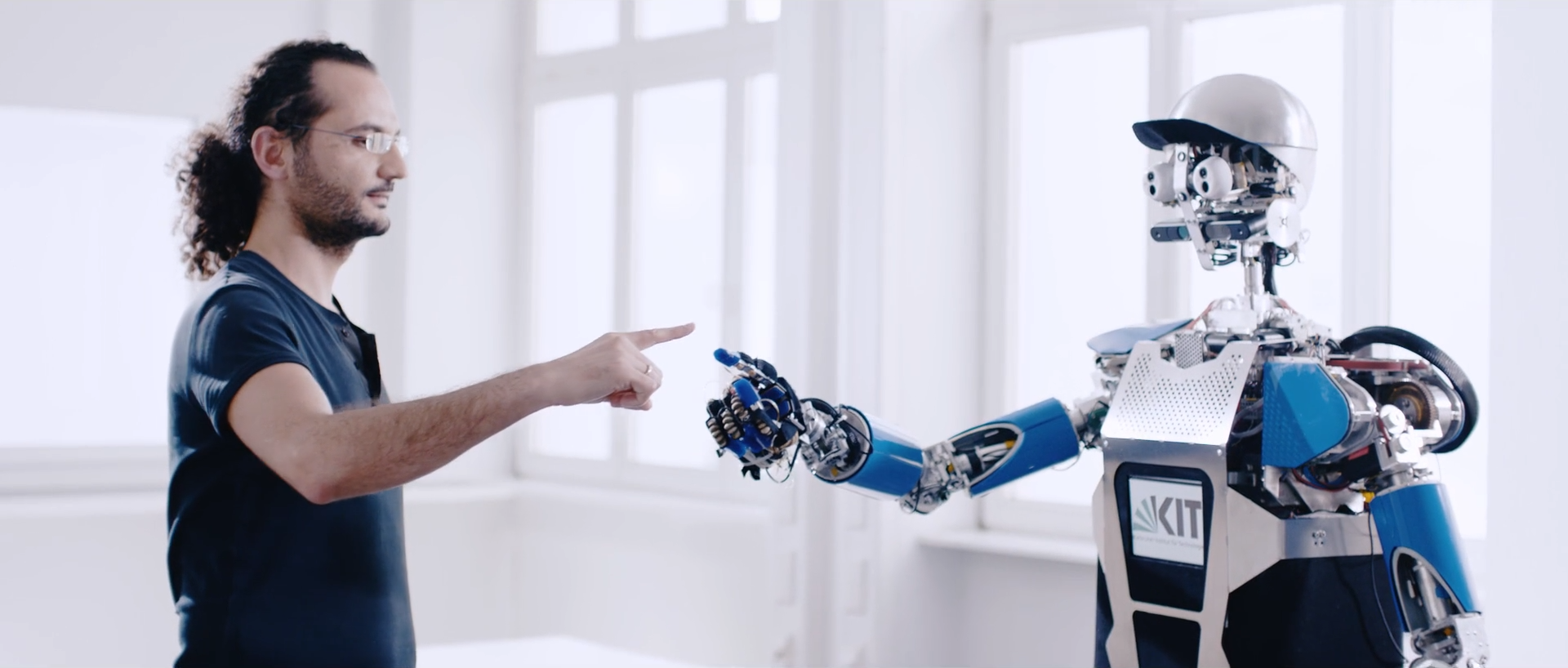 Ein Mensch und ein Roboter strengen die Arme aus und berühren sich fast am Zeigefinger