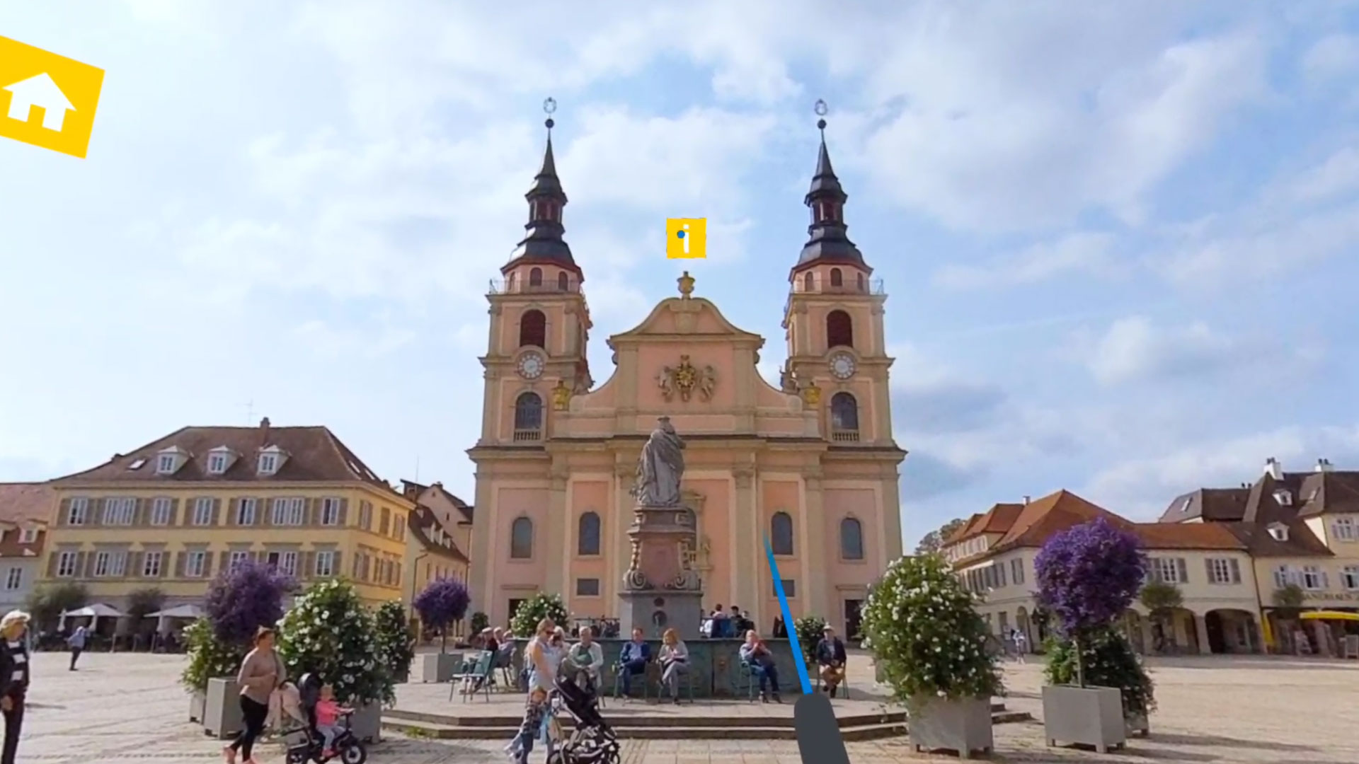 eine lachsrosane Kirche mit zwei spitzen Türmen steht vor einem Brunnen auf einem Marktplatz