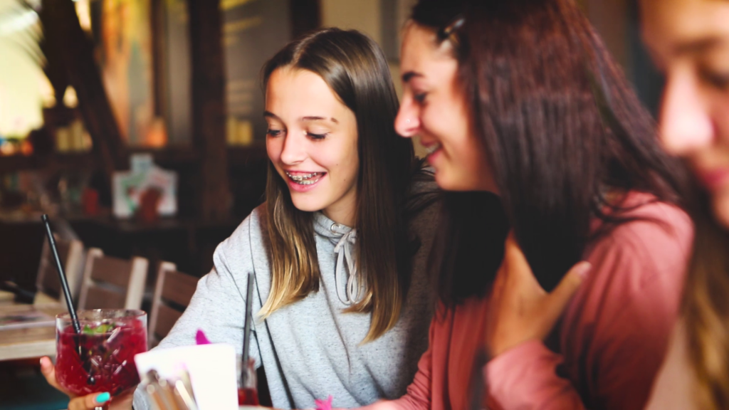 Zwei Mädchen lachen an einem Restauranttisch und schauen auf ein Handy